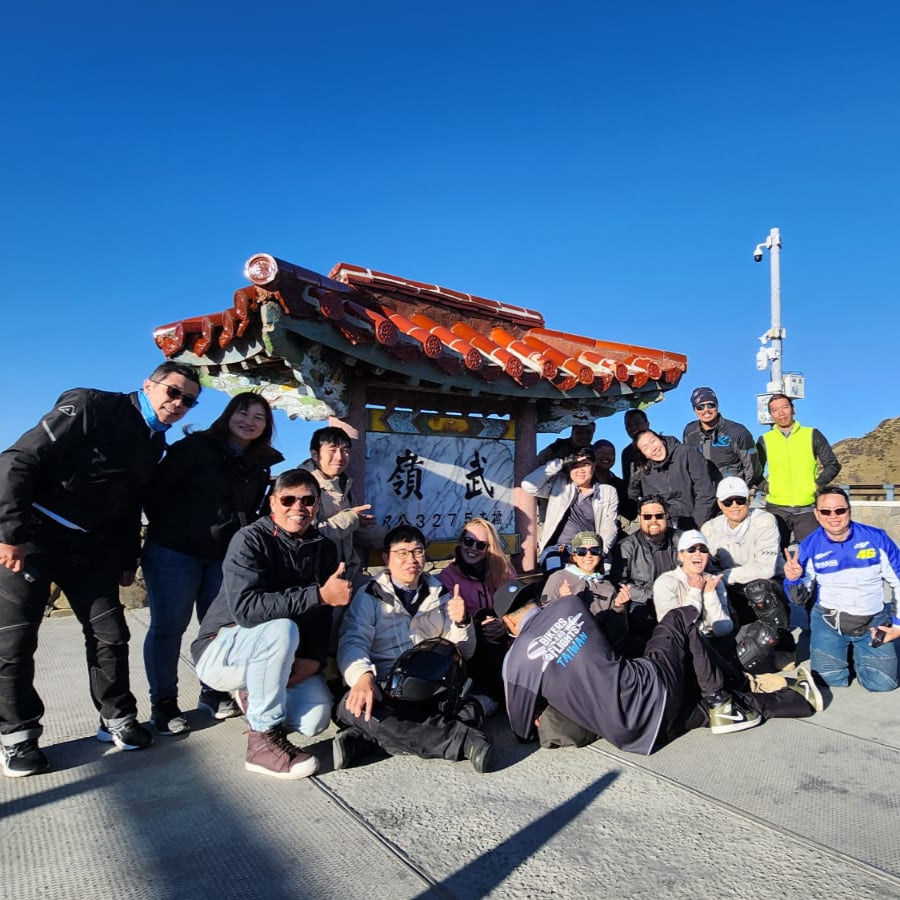 Group of people posing for a photo on a scenic overlook with mountains in the background.